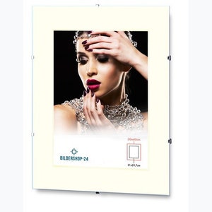 Könnte beinhalten: Ein weißer Bilderrahmen mit einem cremefarbenen Passepartout. Der Rahmen hat eine klare Acrylglasfront und einen silbernen Metallrahmen. Der Rahmen hängt an einer weißen Wand. Das Bild im Rahmen zeigt eine Frau mit langen dunklen Haaren, die eine Diamantenkette trägt. Das Bild ist auf Schulterhöhe zugeschnitten. Der Text "BILDERSHOP-24" ist in der linken unteren Ecke des Rahmens gedruckt. Der Text "30x40cm" ist in der rechten oberen Ecke des Rahmens gedruckt. Der Text "21x29,7cm" ist in der rechten unteren Ecke des Rahmens gedruckt.