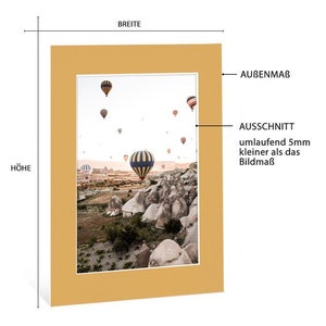 May include: A yellow frame with a photo of hot air balloons flying over a rocky landscape. The photo is titled "Ausschnitt umlaufend 5mm kleiner als das Bildma&szlig;".