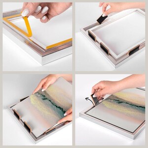 May include: A step-by-step guide on how to use adhesive strips to hang a framed picture. The first image shows a person applying adhesive strips to the back of a silver frame. The second image shows the adhesive strips attached to the back of the frame. The third image shows a person placing a picture into the frame. The fourth image shows the picture hanging on the wall.