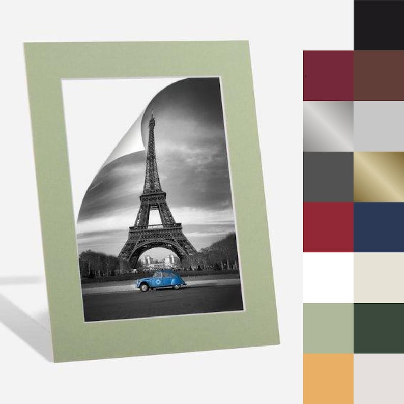 May include: A green mat with a white border surrounds a black and white photo of the Eiffel Tower in Paris, France. A blue car is driving in front of the tower. The photo is slightly curled at the top right corner.