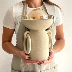 ceramic lamp, porous texture, without lamp shade, it is like a cylinder and on top of it a bowl that has a light bulb inside, you have two rings on the sides that reach almost to the base, they give it originality