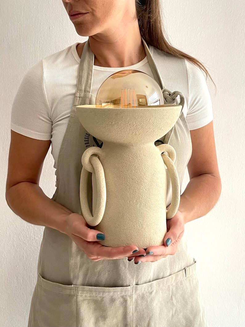 ceramic lamp, porous texture, without lamp shade, it is like a cylinder and on top of it a bowl that has a light bulb inside, you have two rings on the sides that reach almost to the base, they give it originality