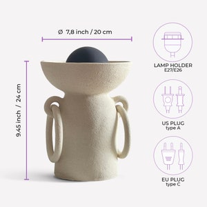 Pu&ograve; includere: Un vaso in ceramica bianca con due manici e una parte superiore rotonda. Il vaso &egrave; alto 24 cm e largo 20 cm. Ha una lampadina nera all'interno. L'immagine mostra anche i diversi tipi di spine disponibili: spina americana, spina europea e portalampada E27/E26.