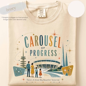 May include: An ivory t-shirt featuring a graphic print with the text Carousel of Progress and There's A Great Big Beautiful Tomorrow. The design includes a mid-century style building, a tower, and three figures standing in front of the structure.