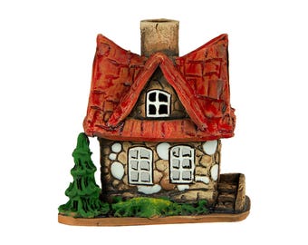 May include: A miniature stone cottage with a red tiled roof, chimney, and small windows. A green tree and grass are at the base of the cottage. The cottage is a decorative item.