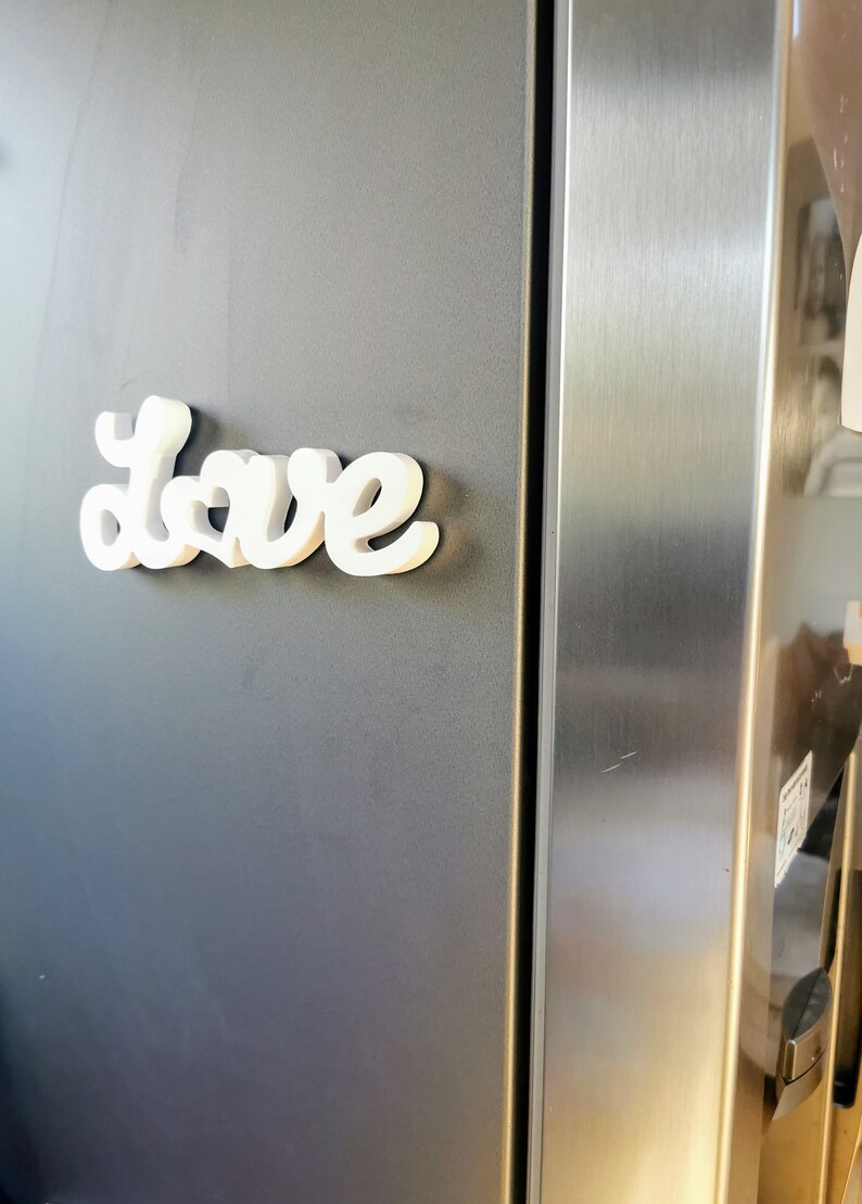 May include: White, three-dimensional letters spelling "Love" are attached to a grey refrigerator door.