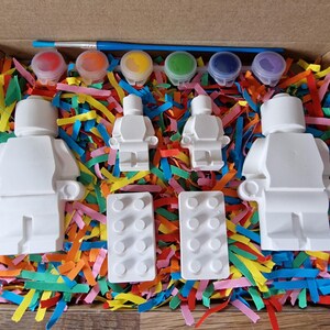 May include: A paint-your-own Lego minifigure set with four white figures, two white Lego baseplates, and six small paint pots with red, orange, yellow, green, blue, and purple paint.
