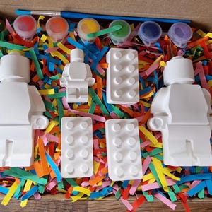 May include: A paint-your-own LEGO&reg; minifigure kit with three white ceramic minifigures, two white ceramic LEGO&reg; bricks, and four small paint pots with red, yellow, green, and blue paint.