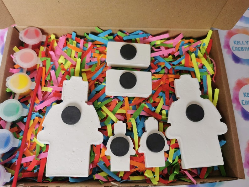 May include: A set of five white ceramic figures with black magnetic circles on the back. The figures are shaped like firefighters and are surrounded by colorful shredded paper. A set of paint pots and a paintbrush are included.