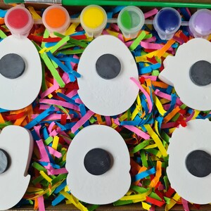 May include: A set of six white ceramic shapes with black magnet circles in the centre, surrounded by colourful shredded paper. The shapes are in a cardboard box with five small paint pots and a paintbrush.
