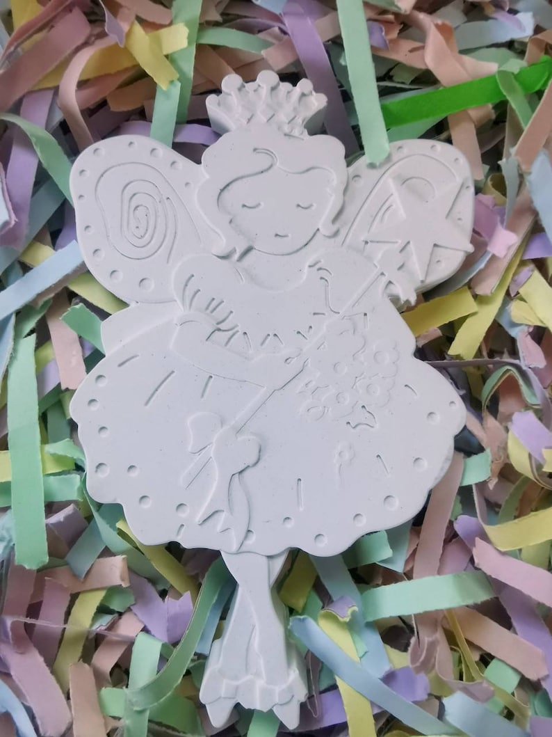 May include: White ceramic fairy figurine with a crown, wings, and a wand. The fairy is wearing a dress with a bow and is holding a bouquet of flowers.