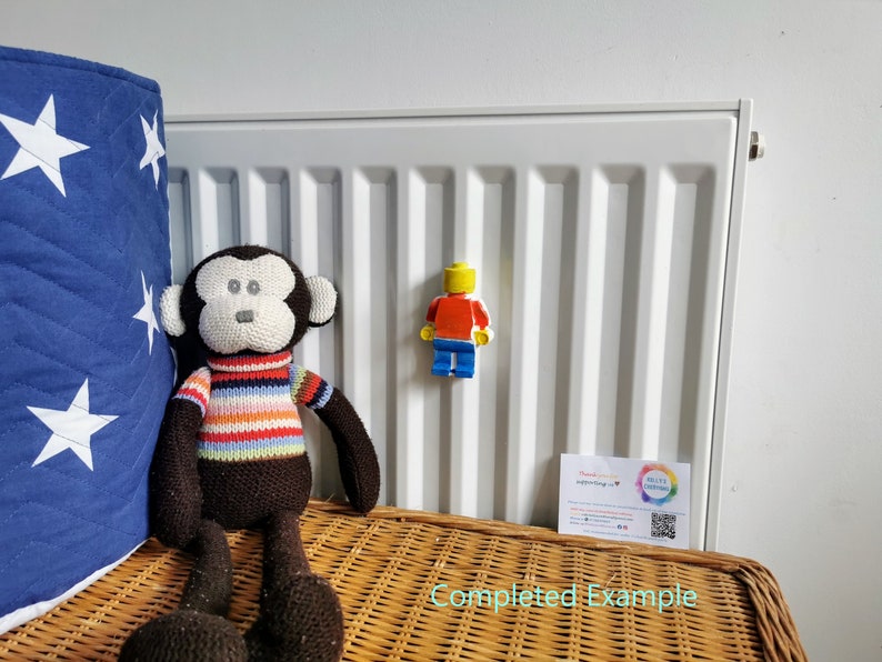May include: A brown and white striped monkey plush toy sits on a wicker surface next to a white radiator. A yellow, red, and blue Lego figurine is attached to the radiator.