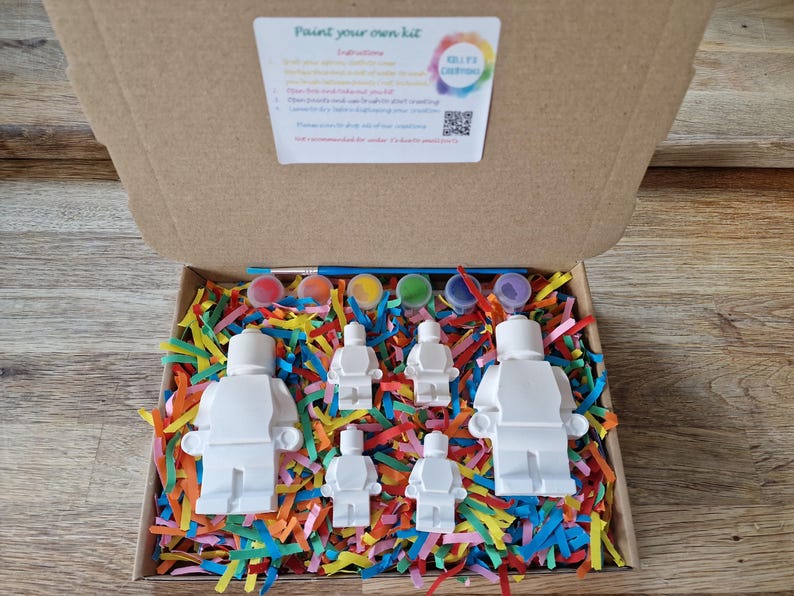 May include: A paint your own kit with five white figurines of people, paint pots, and a paintbrush in a box with colorful shredded paper. The box lid has instructions and the text "Paint your own kit".