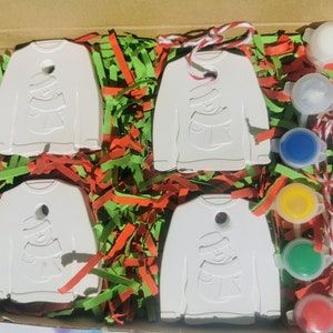 Pu&ograve; includere: Un set di quattro ornamenti in ceramica bianca a forma di maglione con un disegno di pupazzo di neve. Gli ornamenti sono in una scatola con carta triturata rossa e verde. Il set include anche cinque piccoli flaconi di vernice e un pennello.