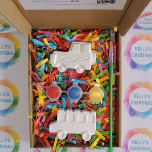 Puede incluir: Un kit de manualidades en una caja de cart&oacute;n. Contiene dos piezas de cer&aacute;mica blancas con forma de veh&iacute;culo, tres botes de pintura roja, azul y amarilla y un pincel verde. La caja est&aacute; llena de papel triturado de colores.