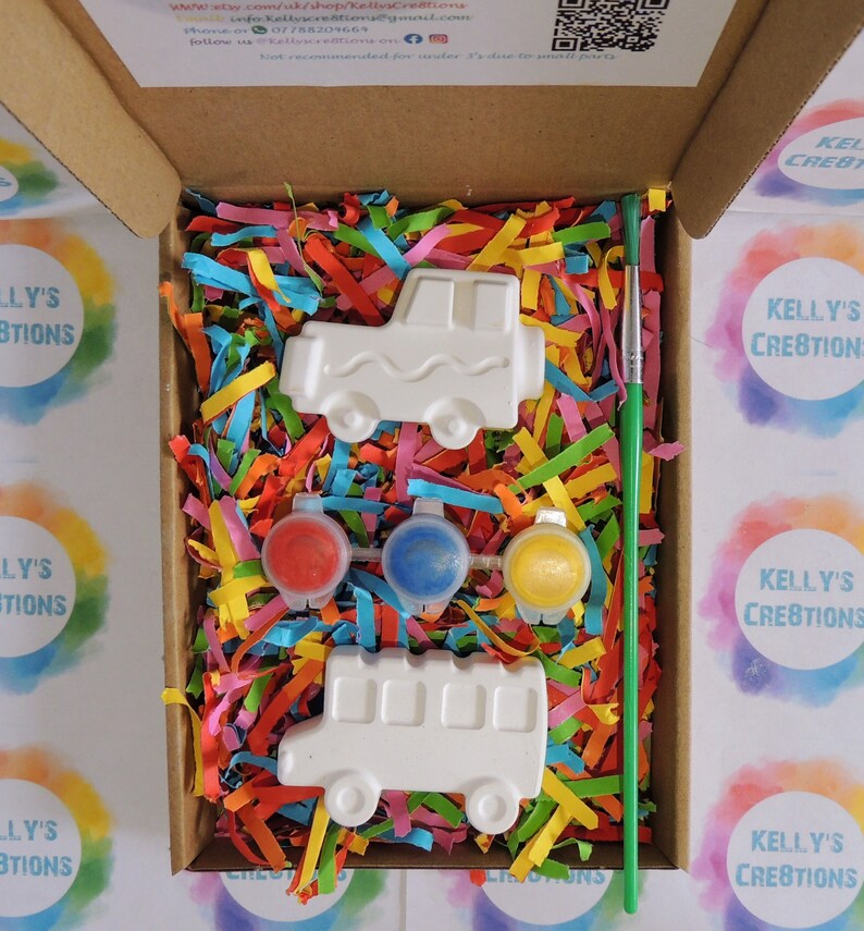 Puede incluir: Un kit de manualidades en una caja de cart&oacute;n. Contiene dos piezas de cer&aacute;mica blancas con forma de veh&iacute;culo, tres botes de pintura roja, azul y amarilla y un pincel verde. La caja est&aacute; llena de papel triturado de colores.