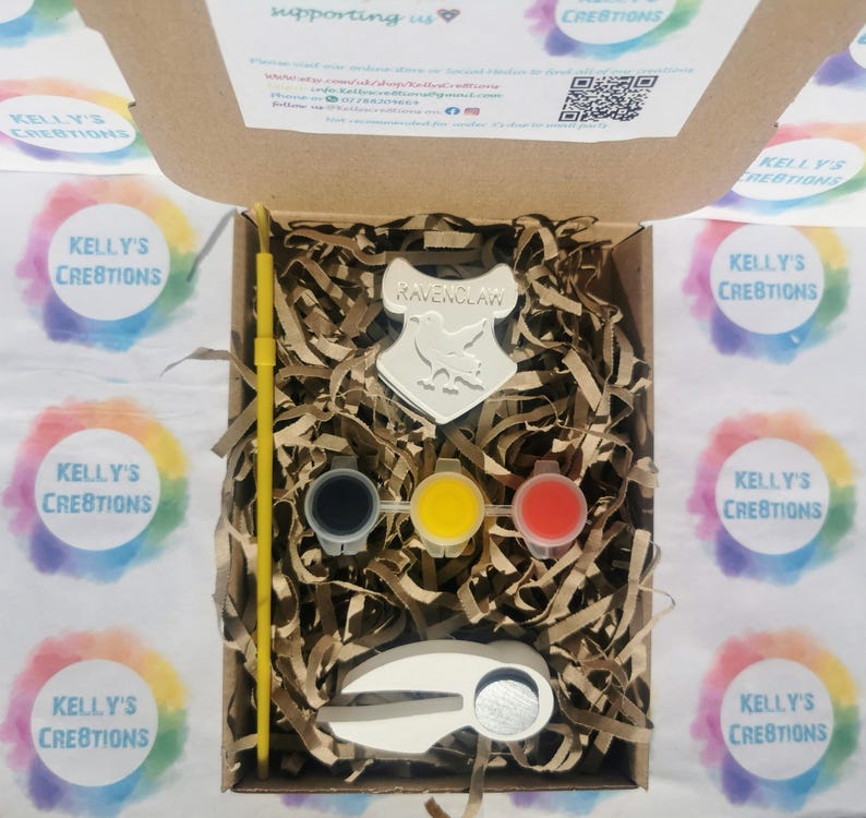 May include: A craft kit with a Ravenclaw crest, paint pots in black, yellow, and red, a paintbrush, and a ceramic item. The kit is in a cardboard box with shredded paper filler. The box is surrounded by stickers with the text "Kelly's Creations".