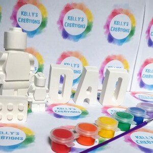May include: A white paint-your-own LEGO&reg; minifigure set with a baseplate and the word "DAD" spelled out in large white letters. The set comes with six small paint pots in various colors.