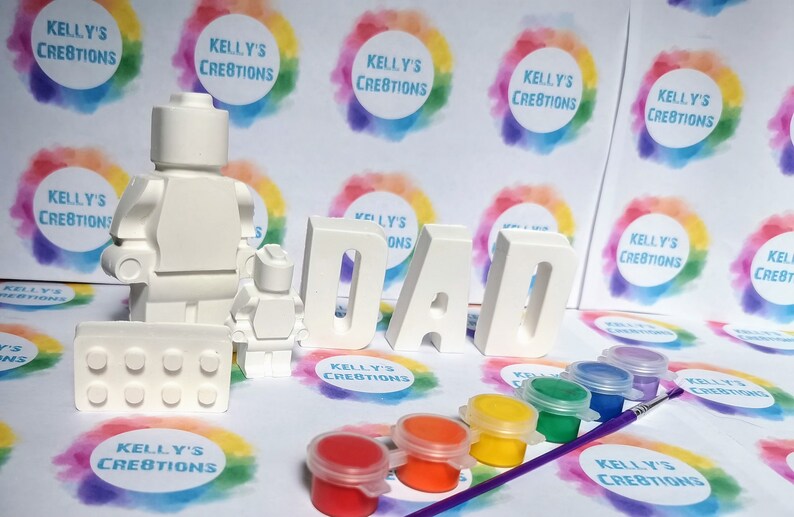 May include: A white paint-your-own LEGO&reg; minifigure set with a baseplate and the word "DAD" spelled out in large white letters. The set comes with six small paint pots in various colors.
