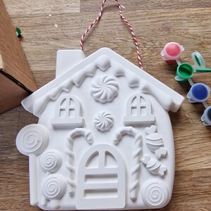 May include: White ceramic gingerbread house ornament with candy cane, lollipop, and swirl designs. The ornament comes with a set of paint pots in red, green, blue, black, and yellow.
