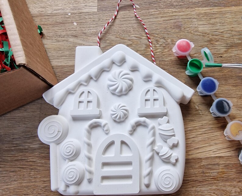 May include: White ceramic gingerbread house ornament with candy cane, lollipop, and swirl designs. The ornament comes with a set of paint pots in red, green, blue, black, and yellow.