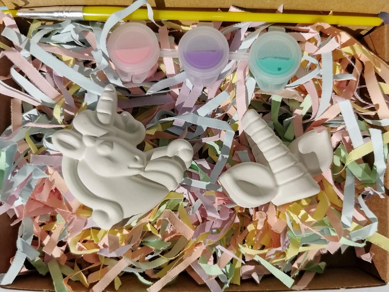 Puede incluir: Un kit de pintura DIY con una figura de unicornio de cer&aacute;mica blanca, un cuerno y una oreja. El kit incluye tres botes de pintura en rosa, morado y turquesa, un pincel y confeti de papel de colores. Los art&iacute;culos est&aacute;n empaquetados en una caja de cart&oacute;n.