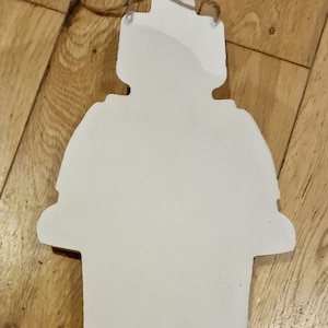 May include: White wooden cutout of a snowman with a round head, a round body, and two arms. The snowman has a rope loop at the top for hanging.