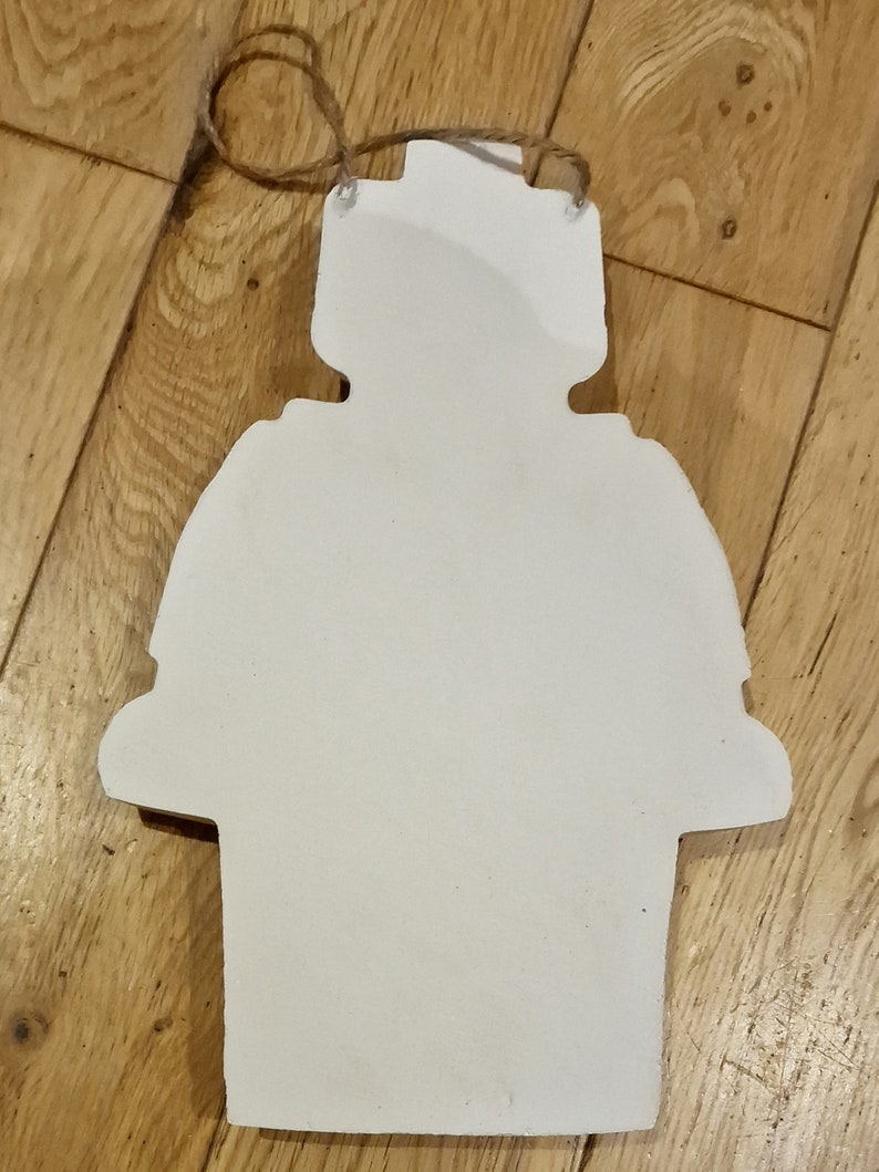 May include: White wooden cutout of a snowman with a round head, a round body, and two arms. The snowman has a rope loop at the top for hanging.