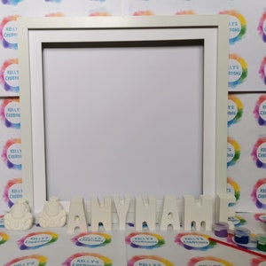 May include: A white wooden frame with a blank canvas inside. Below the frame are white 3D letters spelling "ANYNAME" and two white ceramic figurines. There are also small containers of paint and paintbrushes.
