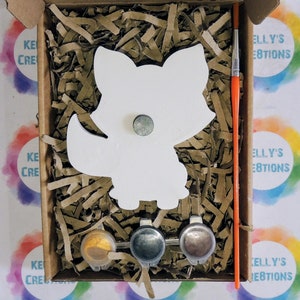 May include: A paint-your-own fox craft kit with three paint pots, a paintbrush, and a white wooden fox cutout. The kit is packaged in a brown cardboard box with the words "Kelly's Creations" printed on the side.