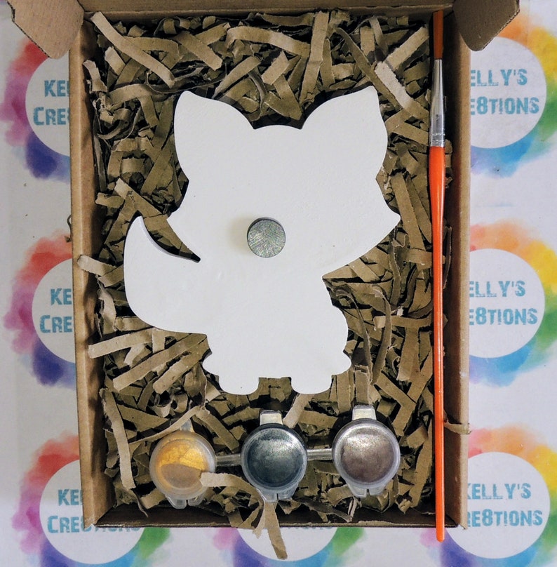 May include: A paint-your-own fox craft kit with three paint pots, a paintbrush, and a white wooden fox cutout. The kit is packaged in a brown cardboard box with the words "Kelly's Creations" printed on the side.