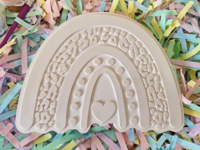 May include: Off-white, unfinished rainbow-shaped craft. The top layer features a leopard print design. The middle layer has a series of dots, and the bottom layer has a heart shape. A craft project for painting.