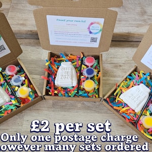 May include: Three brown cardboard boxes containing a white plaster sweatshirt figurine embossed with the text Class of 2026, a black paintbrush, and three small circular pots of red, blue, and yellow paint nestled in colorful paper shreds.