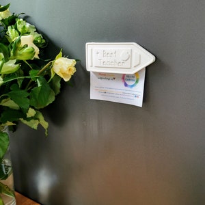 May include: White ceramic pencil magnet with the text "Best Teacher" and a red apple. The magnet is holding a business card that says "Kelly's Creations" and "Thank you for supporting us".