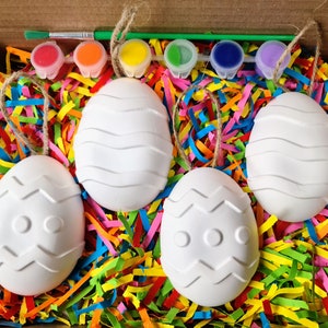 Puede incluir: Un conjunto de cuatro huevos de Pascua de cer&aacute;mica blanca con diferentes dise&ntilde;os en relieve, listos para ser pintados. Los huevos est&aacute;n anidados en papel de colores triturado y vienen con cinco peque&ntilde;os frascos de pintura y un pincel.