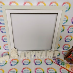 May include: A cream-colored picture frame with a train and the word "ANYNAME" in separate letters. Small paint pots, a paintbrush, and colorful paper strips are also included. The background features a repeating logo with the text "KELLY'S CREATIONS".