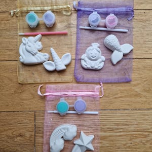 Puede incluir: Tres bolsas de organza llenas de kits de cer&aacute;mica para pintar. Los kits incluyen dos peque&ntilde;os botes de pintura, un pincel y una figurita de cer&aacute;mica. Las figuritas son un unicornio, una sirena y un arco&iacute;ris y una estrella.