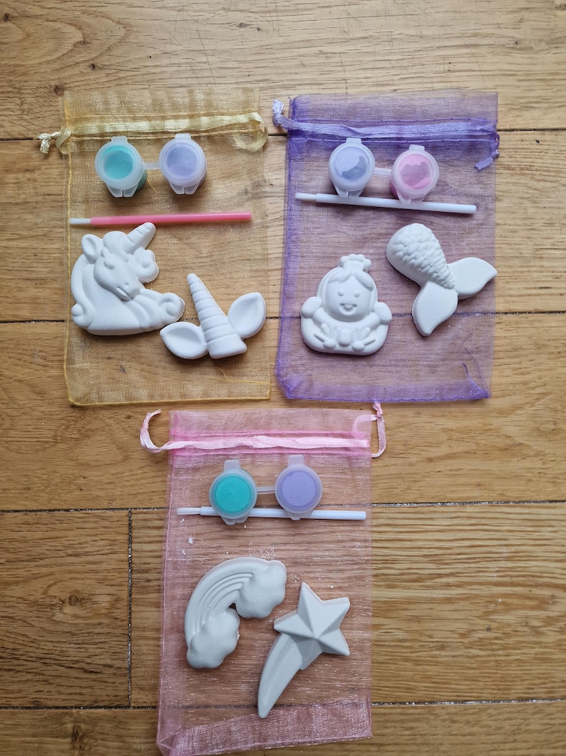 Puede incluir: Tres bolsas de organza llenas de kits de cer&aacute;mica para pintar. Los kits incluyen dos peque&ntilde;os botes de pintura, un pincel y una figurita de cer&aacute;mica. Las figuritas son un unicornio, una sirena y un arco&iacute;ris y una estrella.