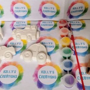May include: A craft kit with four white ceramic cars, a set of six paint pots, a paintbrush, and colorful shredded paper in a box. The cars are ready to be painted.