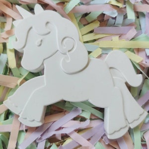 May include: A white, three-dimensional unicorn figurine with a horn, mane, and tail. The unicorn is set against a background of pastel-colored paper strips. The figurine is a blank canvas, ready for painting or decorating.