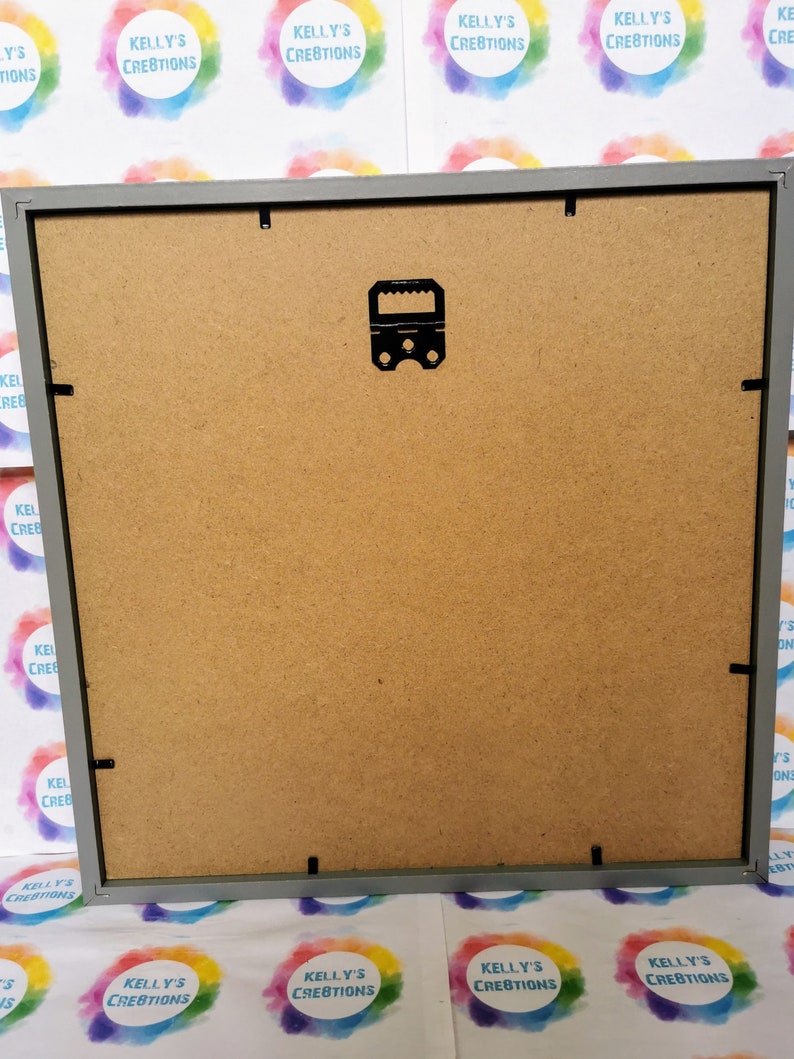 May include: The back of a gray picture frame with a black hanging hook. The frame is made of wood and has a brown cardboard backing.