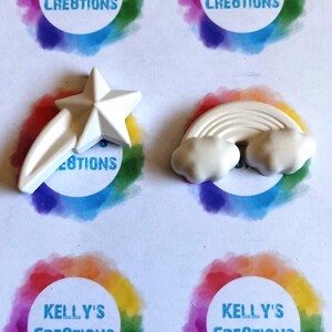 May include: Two white ceramic ornaments, a shooting star and a rainbow with clouds. The ornaments are blank and ready to be painted.