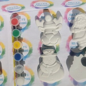 May include: A paint-your-own Christmas craft kit featuring a reindeer, snowman, and Santa Claus figurine. The kit includes a set of paint pots in various colors and the text "KELLY'S CREBTIONS" on the packaging.