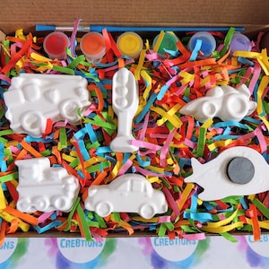 May include: A craft kit with white ceramic car, truck, and traffic light shapes in a box with colorful shredded paper. The kit includes paint pots and paintbrushes.