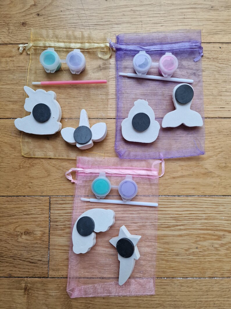 Puede incluir: Tres juegos de adornos para pintar en bolsas de organza. Cada juego incluye dos peque&ntilde;os frascos de pintura, un pincel y una variedad de adornos de cer&aacute;mica. Los adornos incluyen un unicornio, una sirena, una corona, un arco&iacute;ris y una estrella.