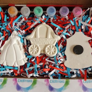 Pu&ograve; includere: Un kit per lavoretti creativi con tre figurine in ceramica bianca: una principessa, una carrozza e una casetta per uccelli. Il kit include sei piccoli flaconi di vernice e un pennello. Le figurine sono su un letto di carta triturata rosso, bianco e blu.