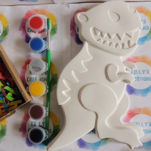 May include: A white ceramic dinosaur figurine with a paint-by-numbers design. The figurine is ready to be painted with the included set of paint pots in red, blue, gray, yellow, brown, and black.