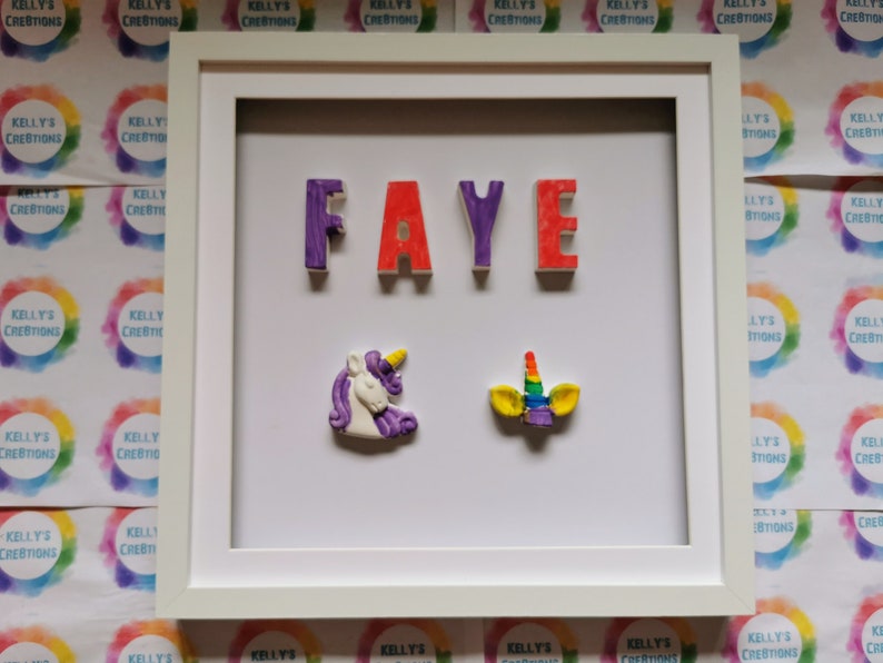May include: A white picture frame with a white mat. The name "FAYE" is spelled out in 3D letters in purple, red, and purple. There are two unicorn decorations, one purple and one rainbow colored.
