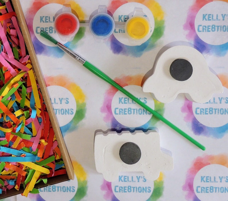 Puede incluir: Un kit de manualidades con pintura, un pincel y dos imanes de cer&aacute;mica sin pintar. El kit incluye pintura roja, azul y amarilla. Los imanes tienen forma de fantasma y cami&oacute;n. El fondo tiene el texto "KELLY'S CREATIONS".