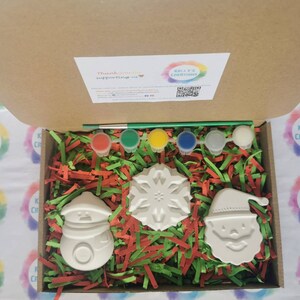 Pu&ograve; includere: Un kit di ceramica fai-da-te a tema natalizio con un pupazzo di neve, Babbo Natale e un fiocco di neve. Il kit include cinque barattoli di vernice, un pennello e carta triturata verde e rossa.
